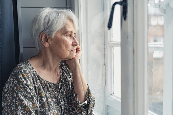 Femme âgée souffrant d'anosognosie regardant par la fenêtre avec un air triste