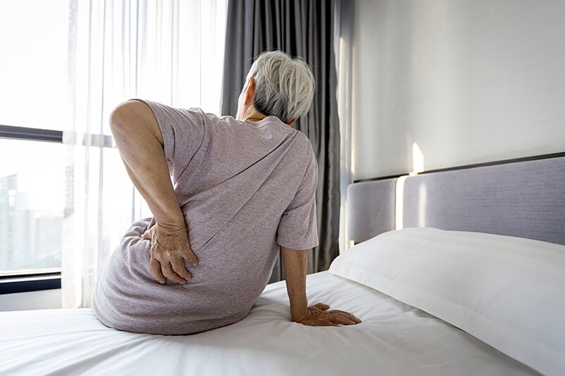 Une personne âgée souffrante de douleurs rénales en raison d'une créatinine élevée, assise sur son lit avec la main sur le dos pour apaiser la douleur.