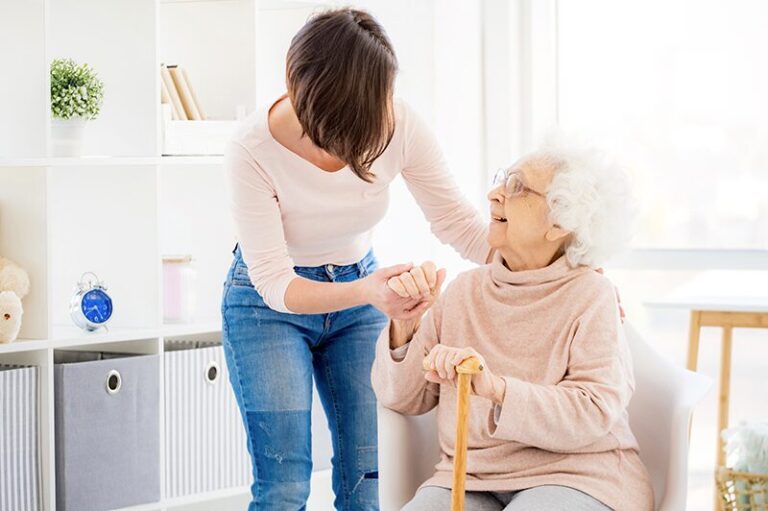 Bientraitance : Une jeune femme qui tient la main d'une personne âgée souriante assise sur son fauteuil roulant