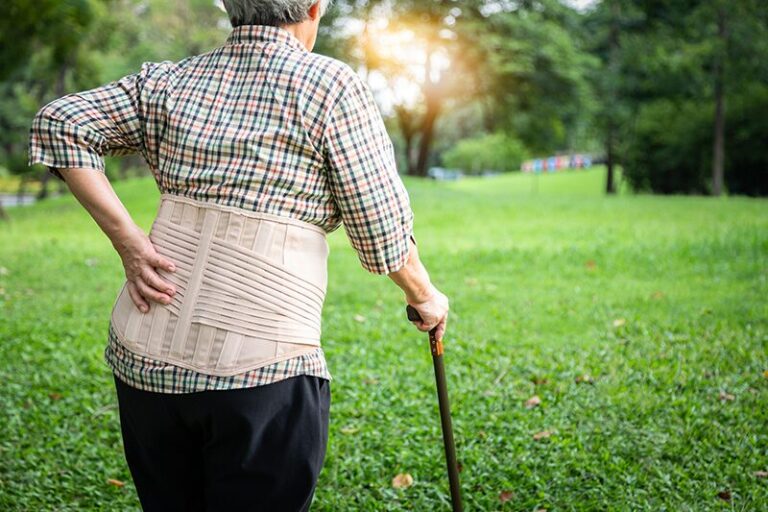 Une femme âgée qui marche difficilement dans un jardin puisqu'elle vient de se faire opérer de la hanche.